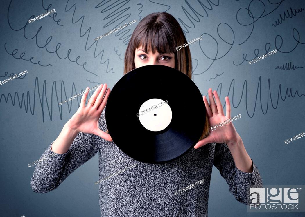Stock Photo: Young lady holding vinyl record on a grey background with scribbles around her.