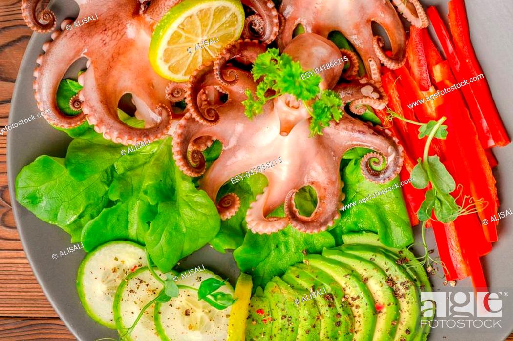 Stock Photo: top down of octopus served with sliced avocado, lettuce, red pepper, lime, cucumber and sprig of pea leaves on plate, restaurant food.