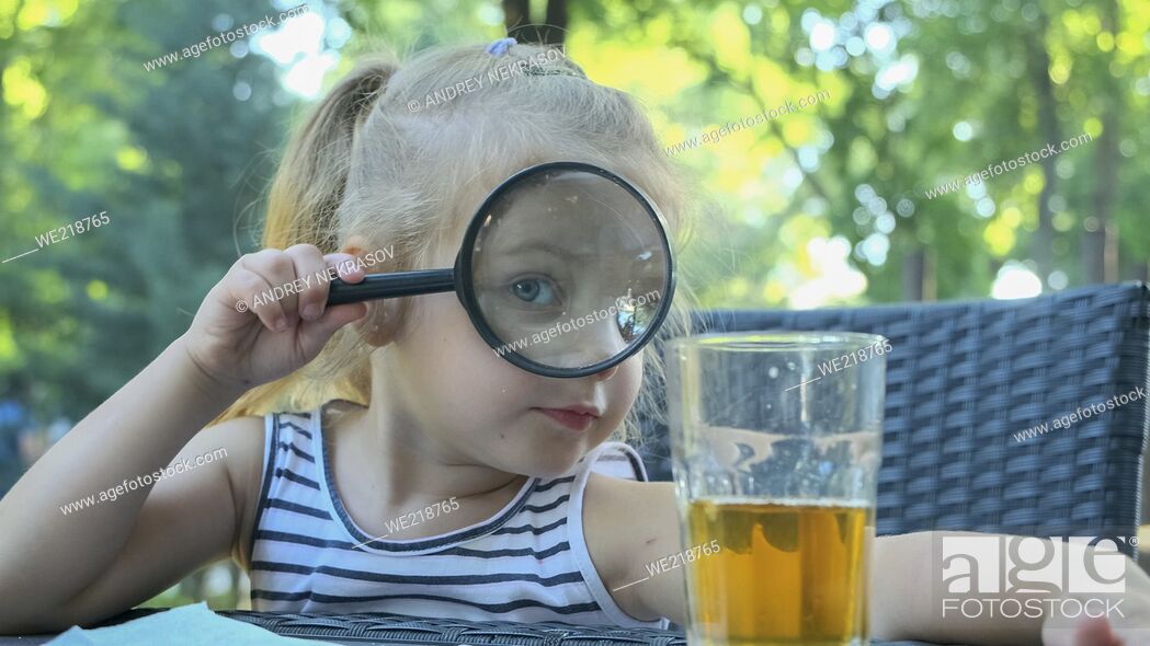 Stock Photo: Little girl looks into the lens around. Close-up of blonde girl studying the world around her looking at it through magnifying glass while sitting in street.