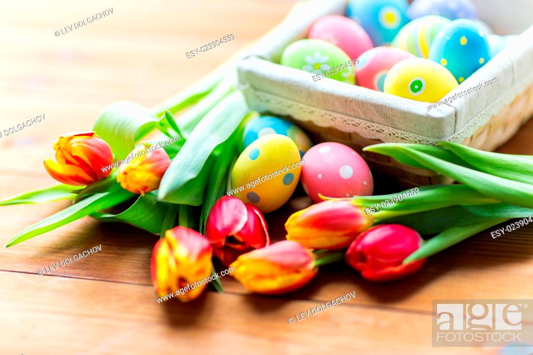 Stock Photo: Easter, holidays, tradition and object concept - close up of colored easter eggs in basket and tulip flowers.