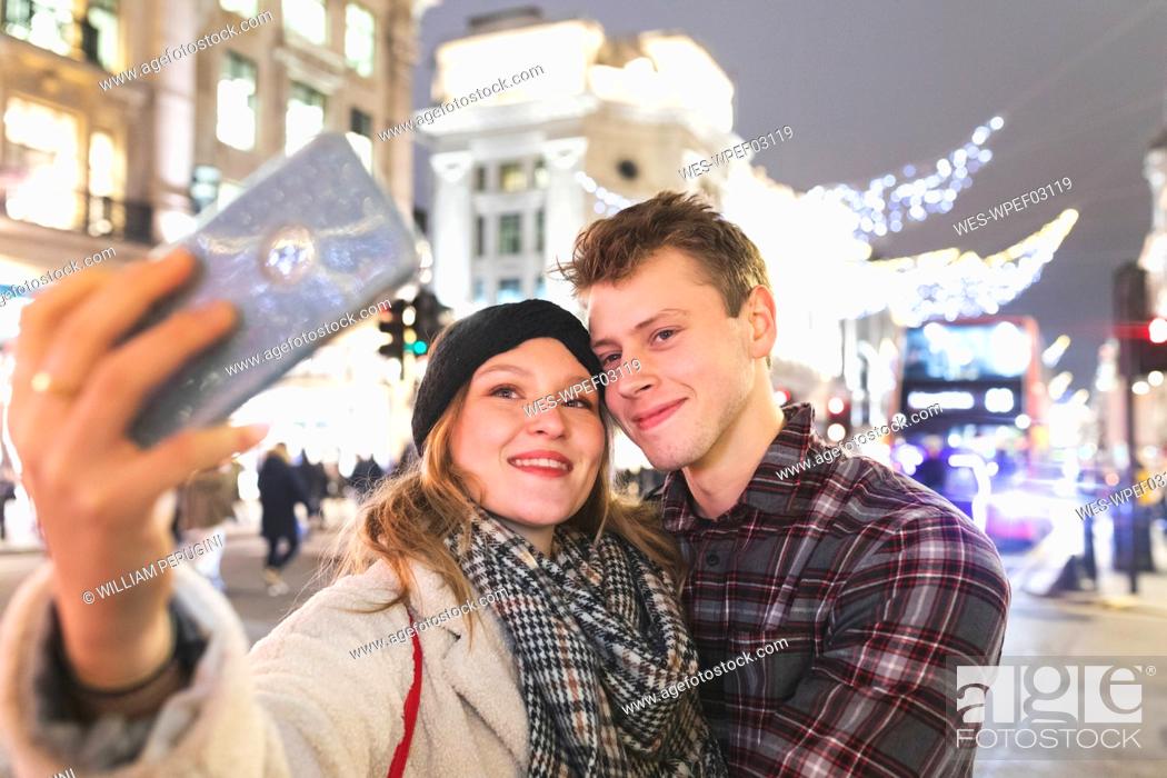 Stock Photo: Woman taking selfie with boyfriend against Christmas lights in city at night.