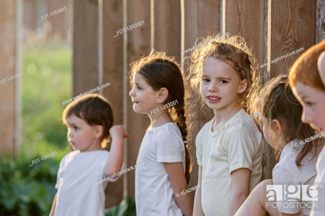 Stock Photo: Portrait of cute girl standing with friends against wooden wall in park.