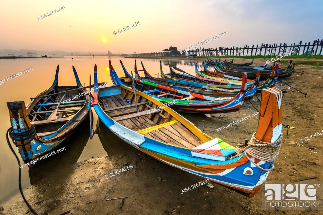 Stock Photo: Amarapura, Mandalay region, Myanmar. Colorful boats moored on the banks of the Taungthaman lake at sunrise, with the U Bein bridge in the background.