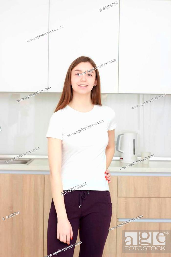 Stock Photo: Pretty young woman In a white T shirt standing in kitchen and smiling. Real interior.