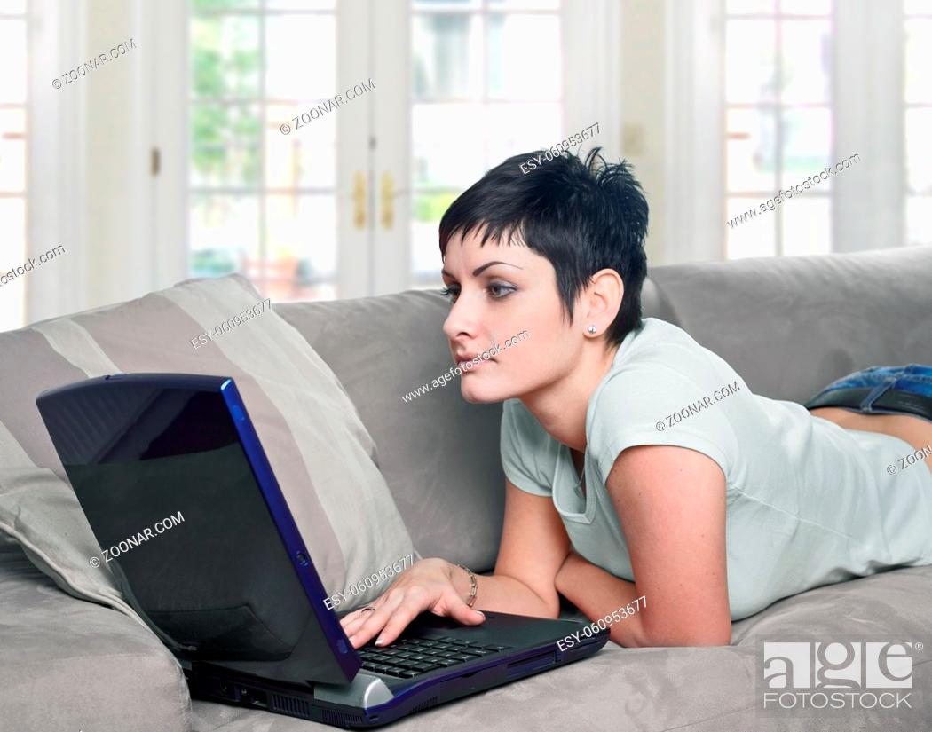 Stock Photo: Young women lies on the sofa at home and works on laptop computer.