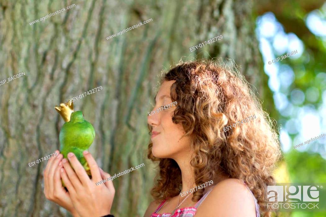 Stock Photo: Teenage Girl Kissing Toy Frog Against Tree Trunk.
