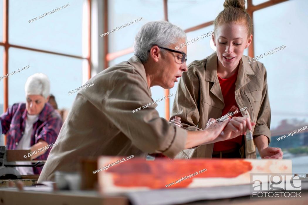 Stock Photo: Mature female carpenter showing wood stain to trainee in furniture making workshop.