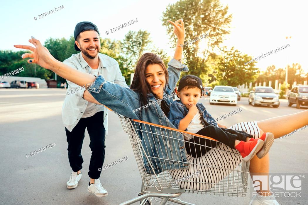 Stock Photo: Young dad carries mom and son in a cart on the parking lot. The family is having fun.