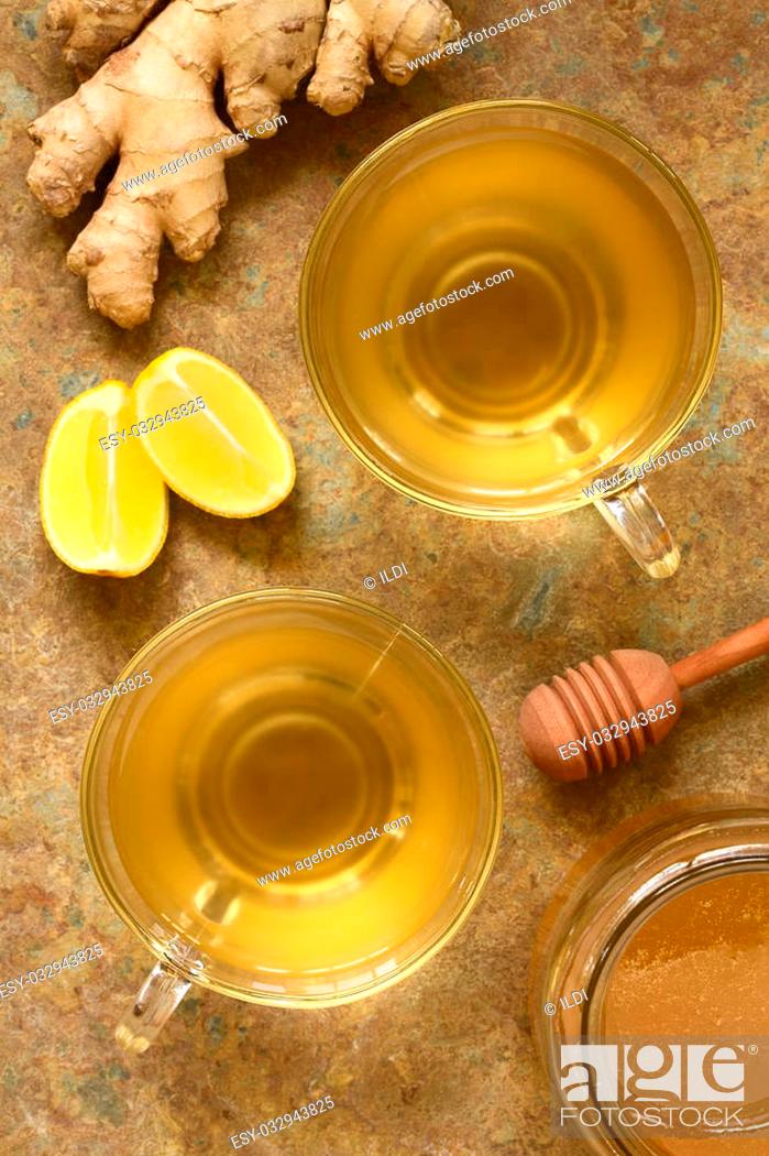 Stock Photo: Hot ginger tea in glass cups with honey, lemon wedges and raw ginger on the side, photographed overhead on slate with natural light (Selective Focus.