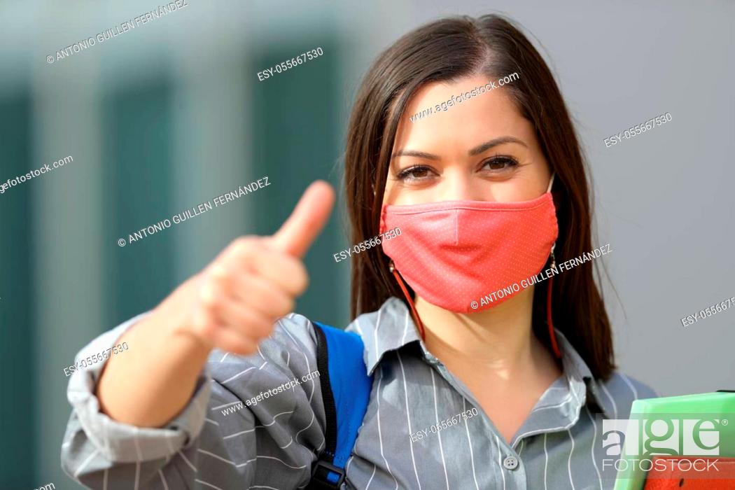 Photo de stock: Front view portrait of a happy student wearing mask with thumbs up in the street.