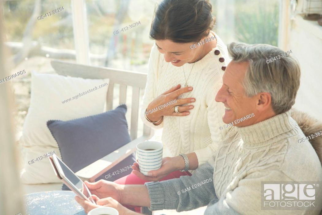 Photo de stock: Mature couple drinking coffee and using digital tablet on porch.