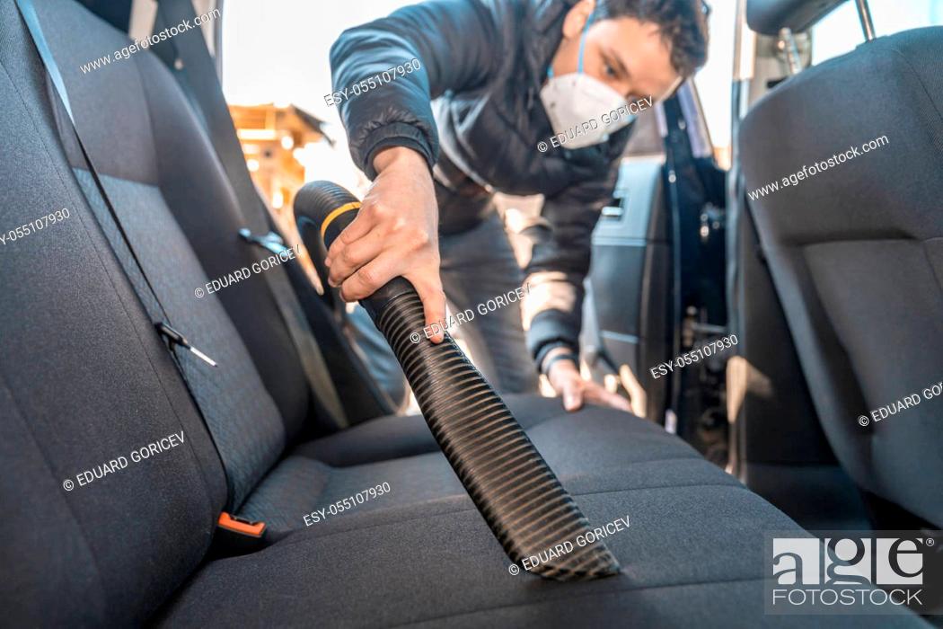 Stock Photo: vacuuming the interior of a car with a respirator on the face during a coronavirus epidemic.