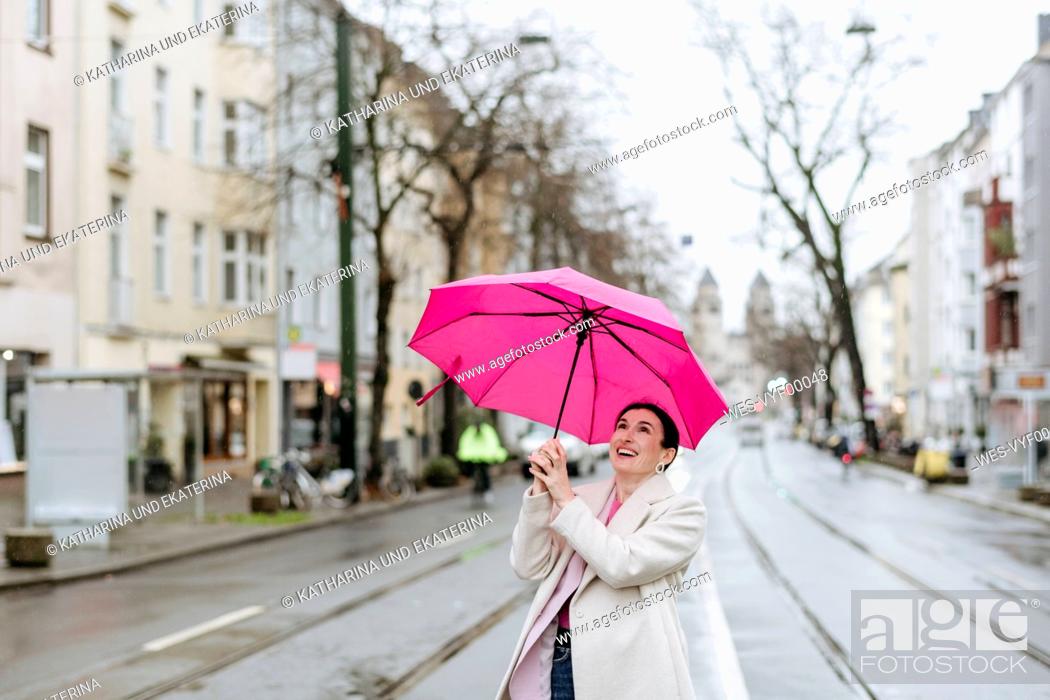 Stock Photo: Smiling woman with pink umbrella walking on street.
