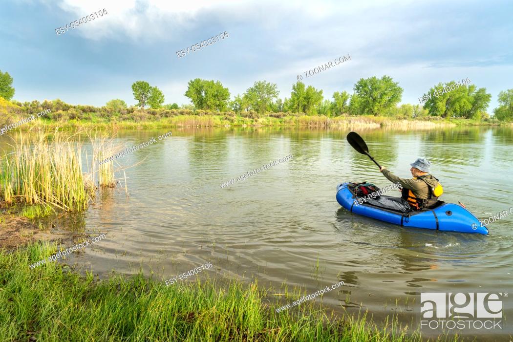 Stock Photo: a senior male paddling a blue pacraft (one-person light raft used for expedition or adventure racing) on a lake in Colorado in springtime scenery.