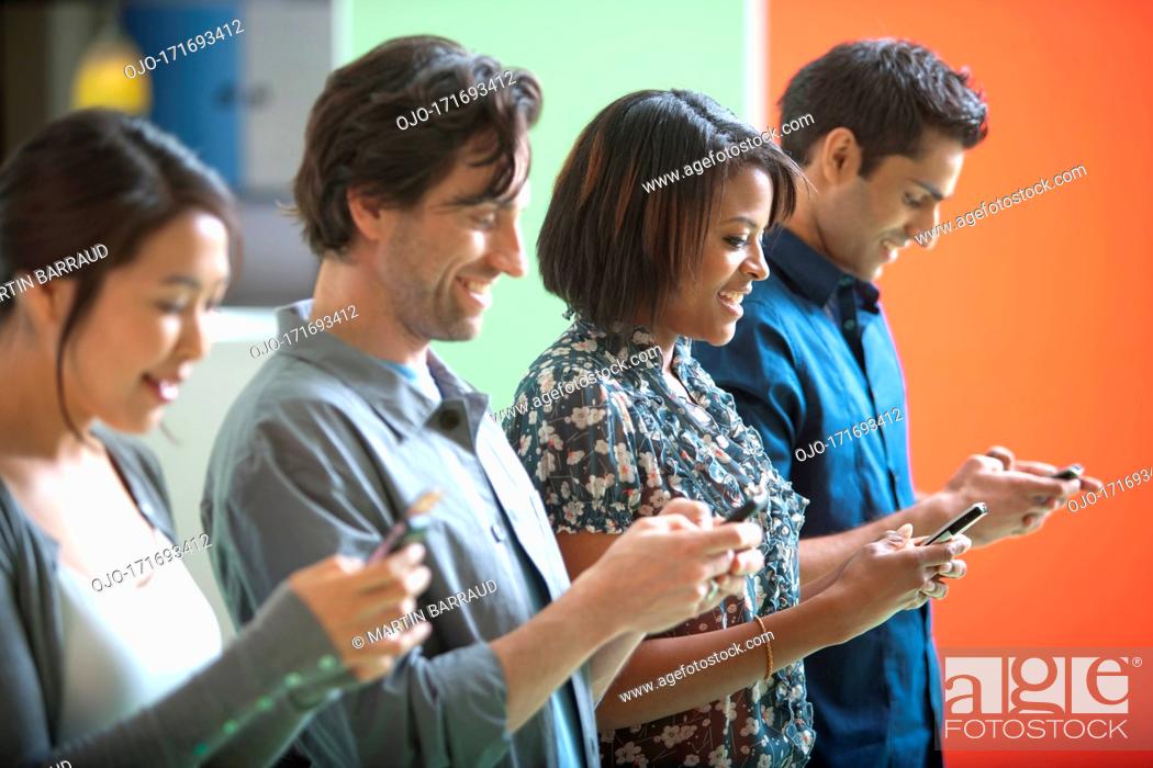 Photo de stock: Smiling men and women text messaging on cell phones in a row.