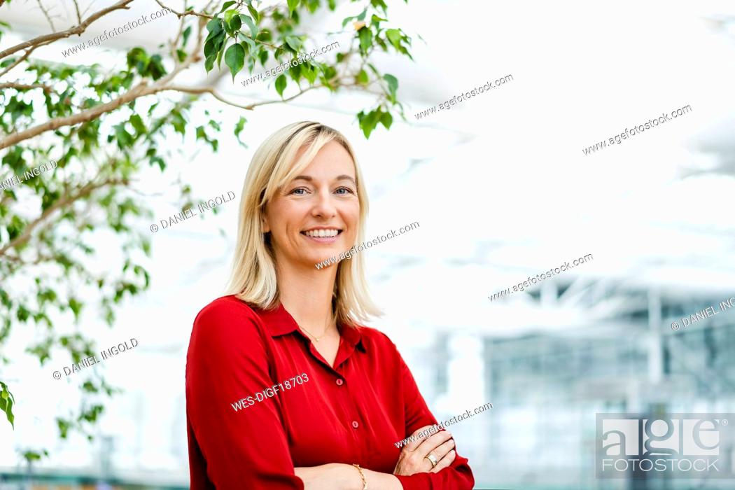Photo de stock: Smiling businesswoman with arms crossed in front of plant.