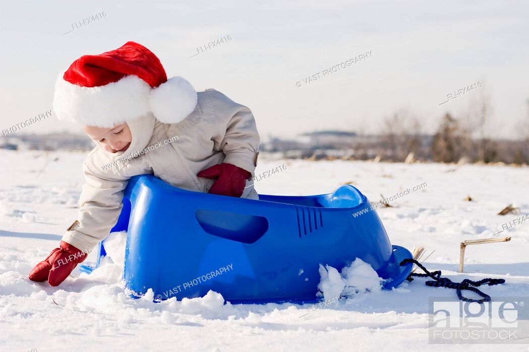 Stock Photo: Boy in Santa Hat Sitting in Sled and Playing with Snow.
