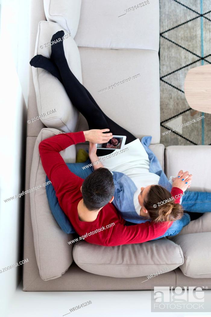 Stock Photo: Young couple relaxing at home using tablet computers reading in the living room on the sofa couch.