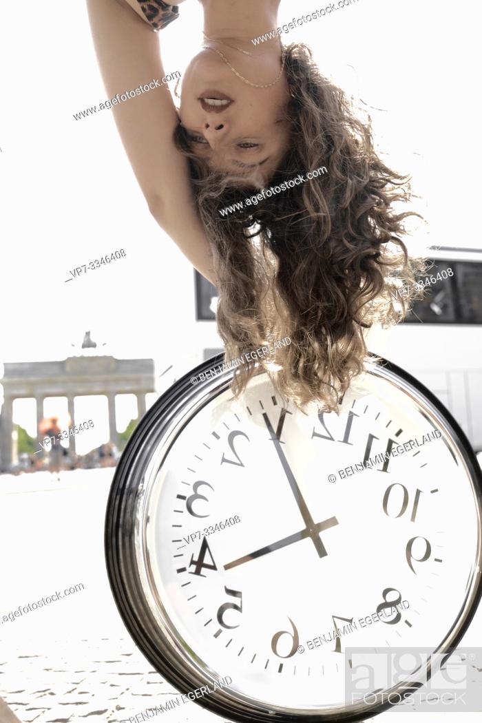 Imagen: young woman upside down with clock at street next to touristic sight Brandenburger Tor, Brandenburg gate, in Berlin, Germany.