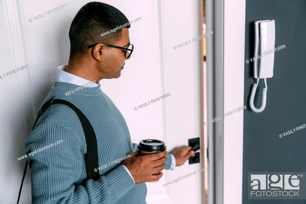 Stock Photo: Young man wearing eyeglasses holding disposable coffee cup opening door.