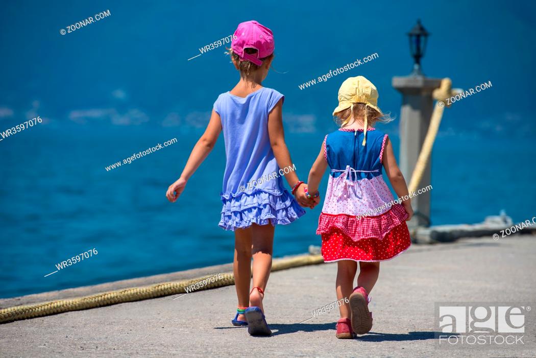 Photo de stock: Happy smiling little sisters having fun holding their hands while walking on the beach coast during Summer vacation Healthy childhood lifestyle concept.