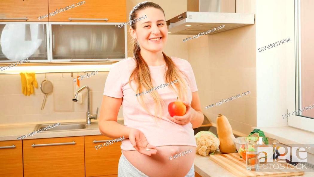 Stock Photo: SMiling young pregnant woman holding vitamin pill and fresh ripe apple in hands. Concept of healthy lifestyle, nutrition and hydration during pregnancy.