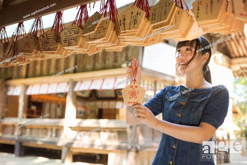 Stock Photo: Young woman wearing blue dress looking at wooden fortune telling plaques at Shinto Sakurai Shrine, Fukuoka, Japan.