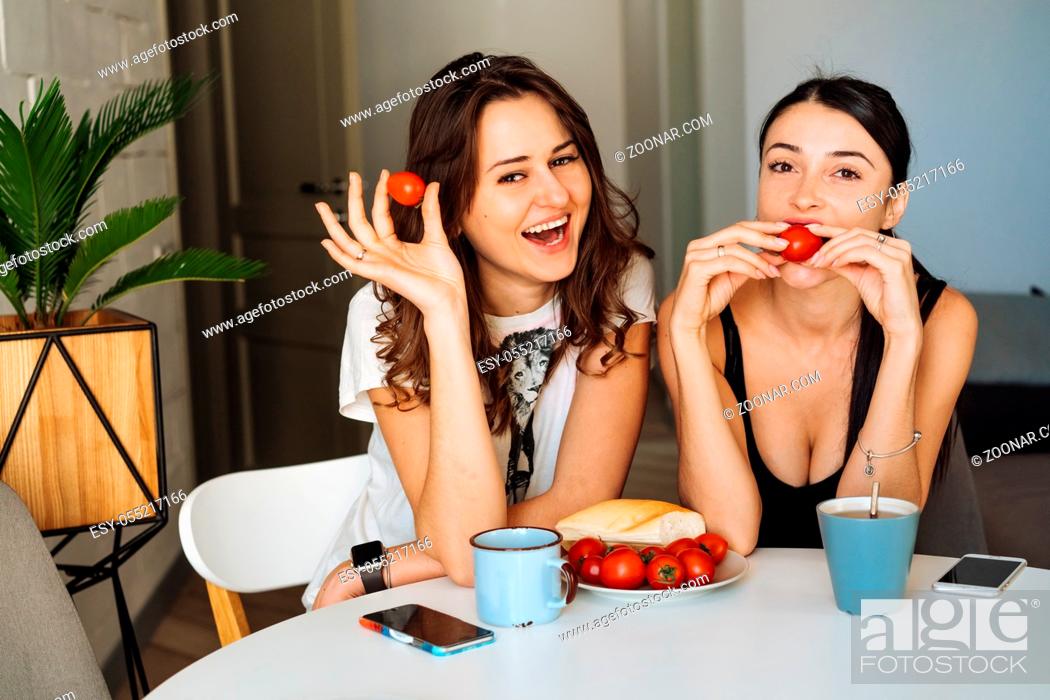 Stock Photo: Two woman friends breakfast in the kitchen and having fun, talking and laughing, sitting at the dining table at home.