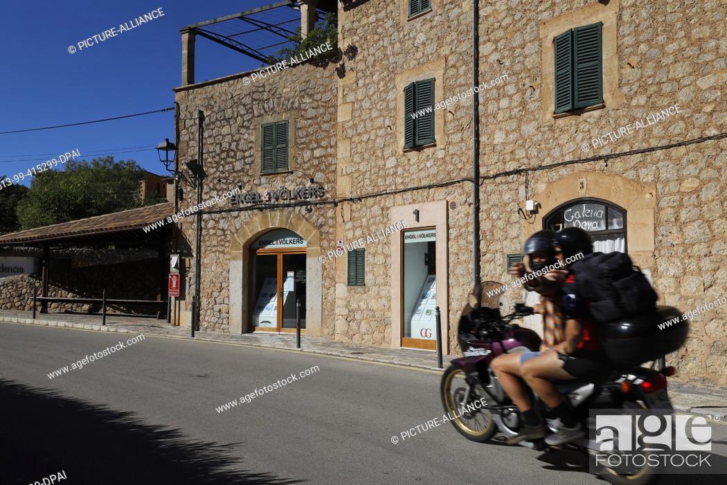 Stock Photo: 13 June 2020, Spain, Deia: A motorcycle passes a real estate agent. The Balearic Islands, which are heavily dependent on tourism.