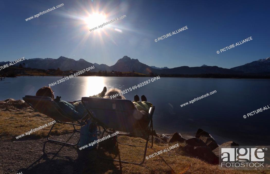 Stock Photo: dpatop - 15 February 2023, Bavaria, Füssen: Two women enjoy the sunshine on deck chairs on the shore of the Hopfensee lake on the edge of the Alps.