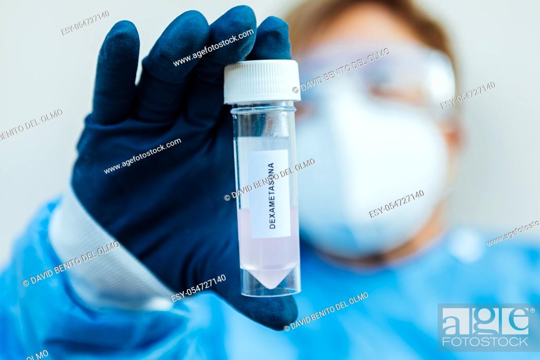 Stock Photo: A biologist wearing gloves, mask, and goggles holds a jar with Dexamethasone in it (covid-19 coronavirus cure).