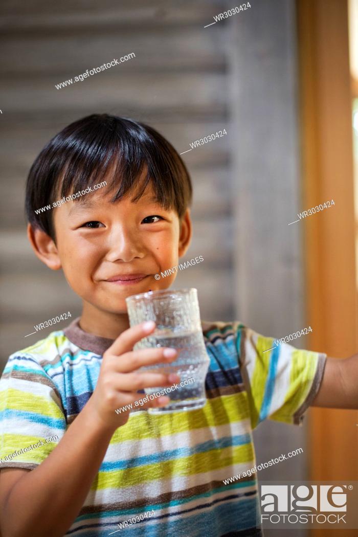 Stock Photo: Portrait of boy with black hair wearing stripy T-shirt, holding drinking glass, smiling at camera.