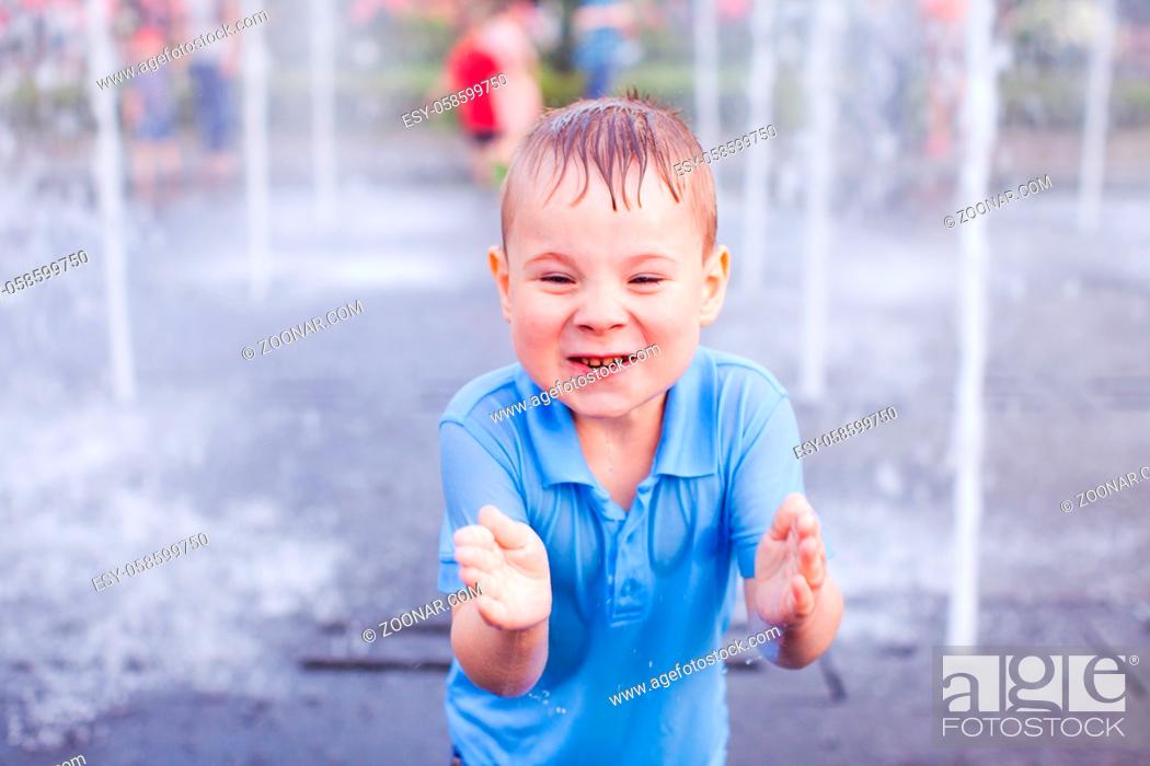 Stock Photo: Funny little boy in a wet blue t-shirt is standing on the background of water splashes.