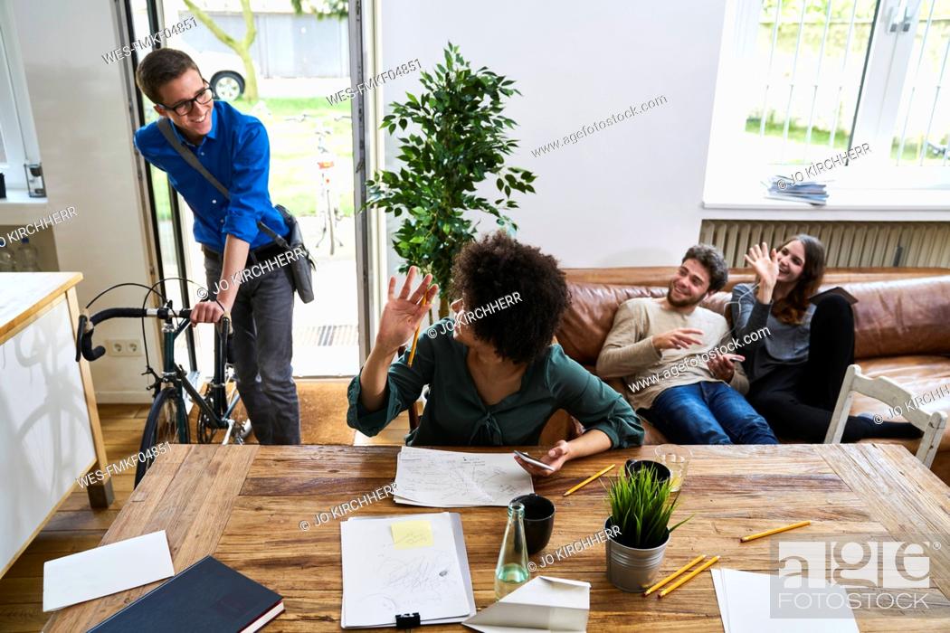 Stock Photo: Coworkers waving at young man with bicycle arriving in modern office.