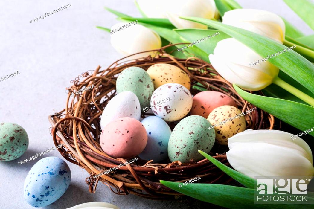 Stock Photo: Beautiful white tulips with colorful quail eegs in nest on light gray stone background. Spring and Easter holiday concept.