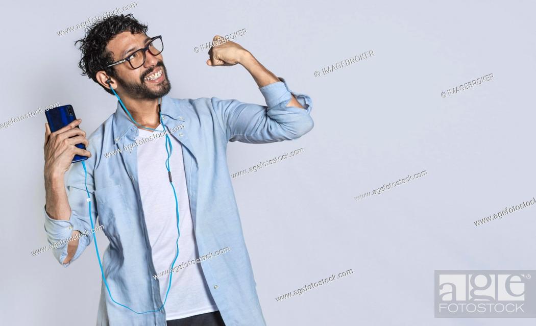 Photo de stock: Happy handsome man with headphones holding a cell phone and celebrating, Happy person using his smartphone and celebrating victory isolated.