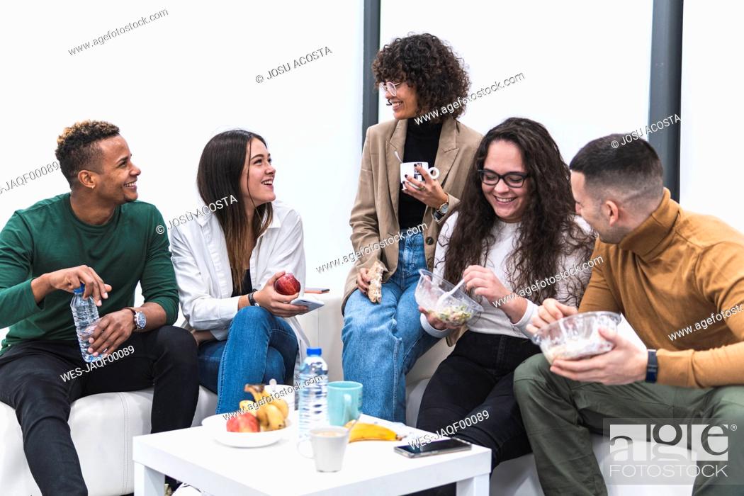 Stock Photo: Smiling male and female colleagues talking while having food and drink in work place canteen.