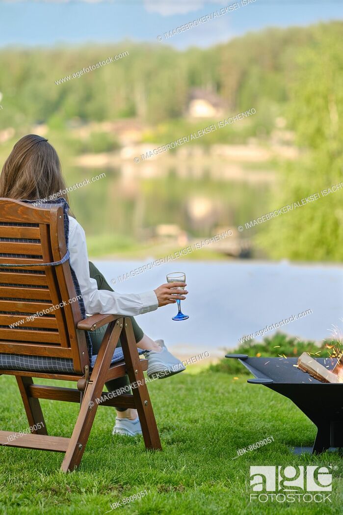 Stock Photo: Young woman with a glass of sangria in her hand relaxes in nature sitting next to a barbecue, back view.