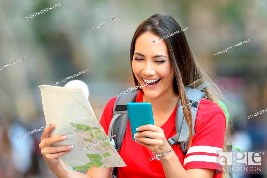 Stock Photo: Happy teen tourist laughing using smart phone and holding a paper map on the street.