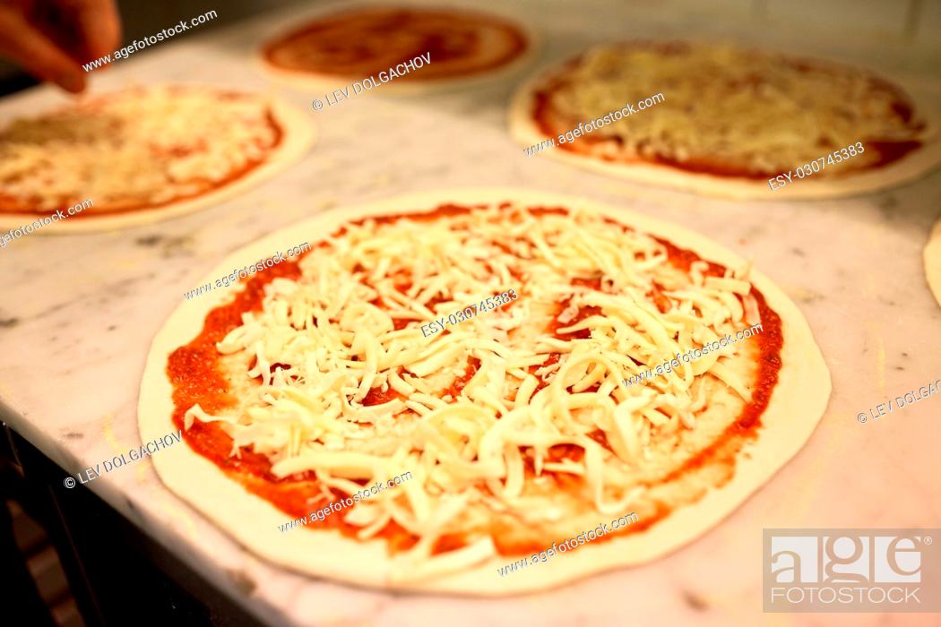 Imagen: food, culinary, italian cuisine and cooking concept - raw pizza with grated cheese on table at pizzeria.