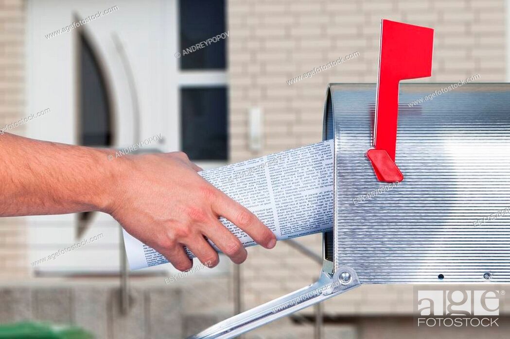 Photo de stock: Man removing a newspaper from his mailbox with a closeup of his hand clasping the folded paper against a blue sky.