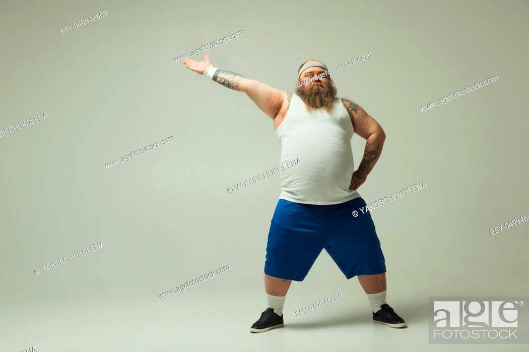 Stock Photo: Do sport. Full length portrait of severe fat man showing by hand aside while standing with arm akimbo. Copy space.
