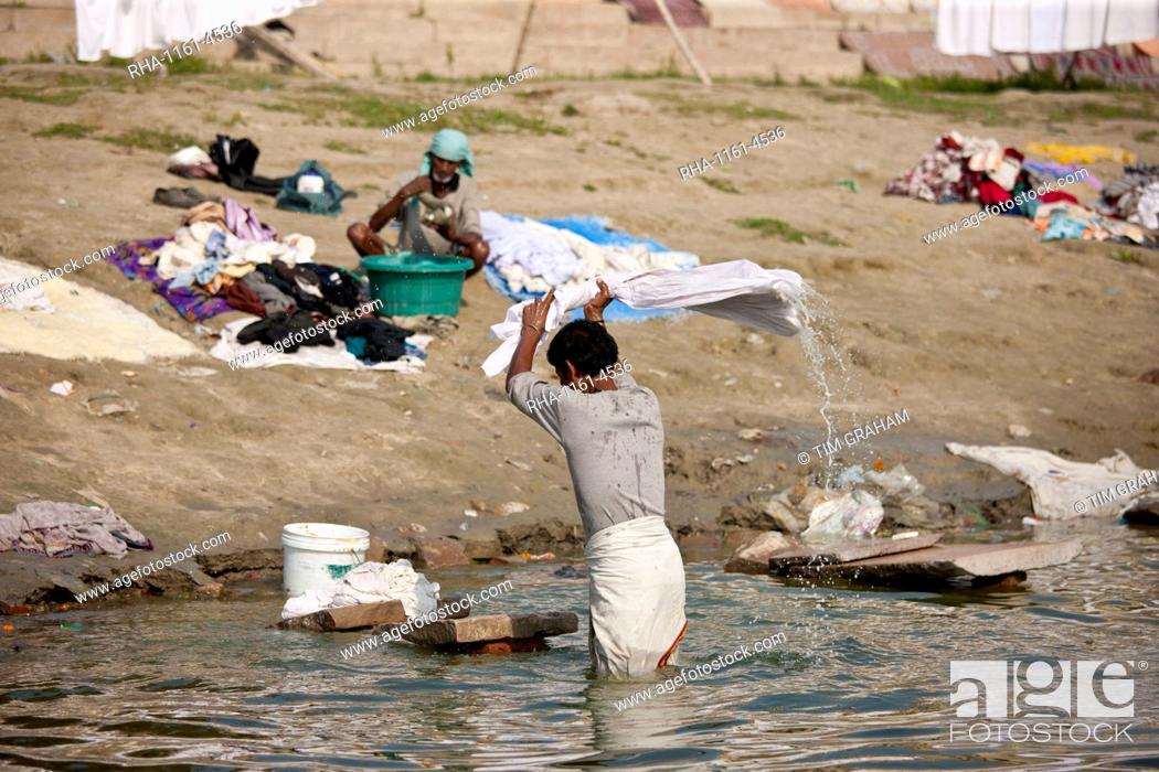 Stock Photo: Indian man doing laundry using flogging stone in waters of The Ganges River at Cabua Pandey Ghat in Varanasi, Benares, India.
