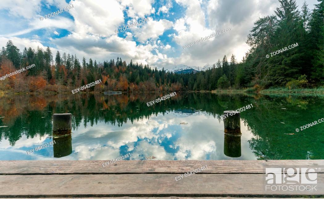 Stock Photo: wooden pier and boardwalk with dock pylons on the edge of an idyllic mountain lake surrounded by fall color forest in the Alps of Switzerland near Flims in the.
