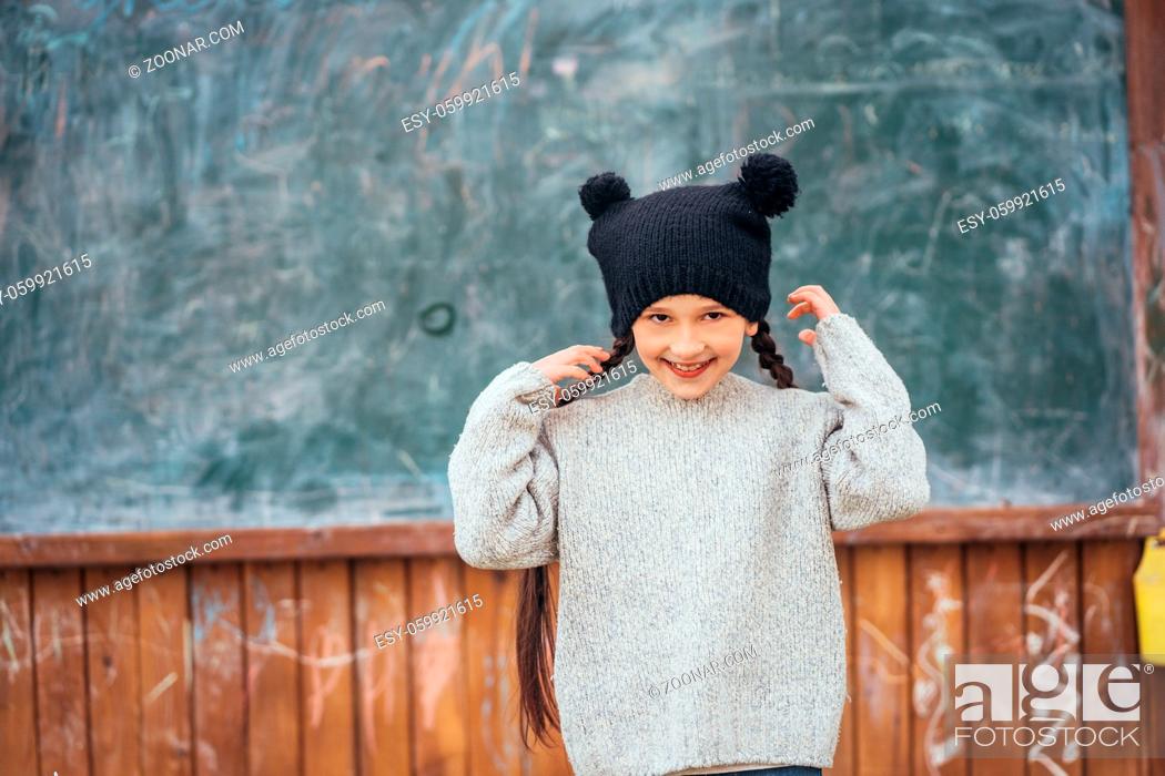 Stock Photo: Little girl in autumn park dressed in a jacket and hat stands at the school board.