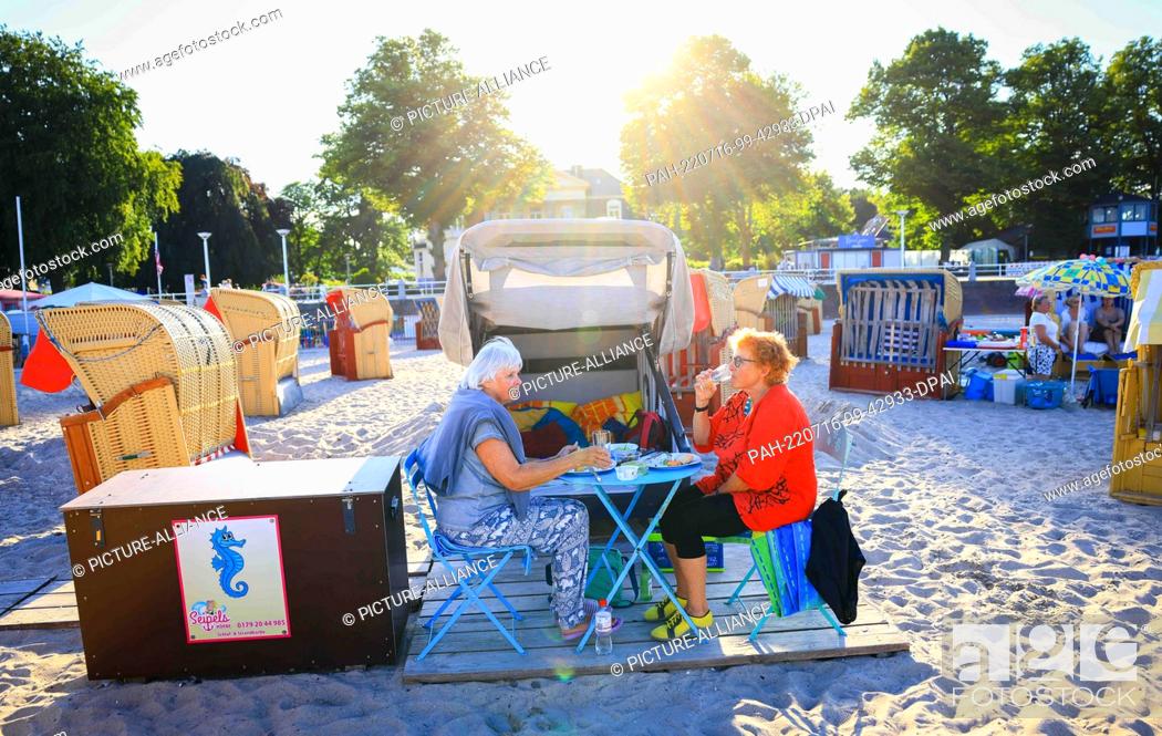 Stock Photo: 14 July 2022, Schleswig-Holstein, Travemünde: Wiltrud Sadlowski (r) and Marion Schleevoight sit in front of their rented sleeping beach chair on the Baltic Sea.