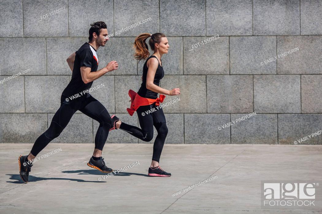 Stock Photo: Side view of people jogging on sidewalk by wall.