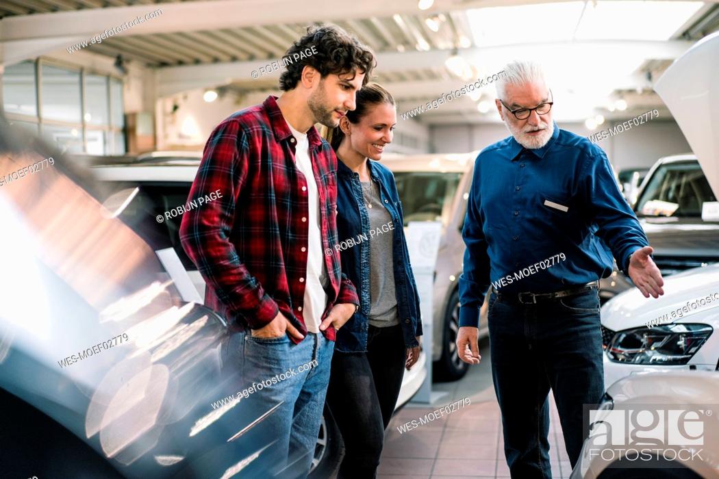 Stock Photo: Car dealer showing car to couple in showroom.