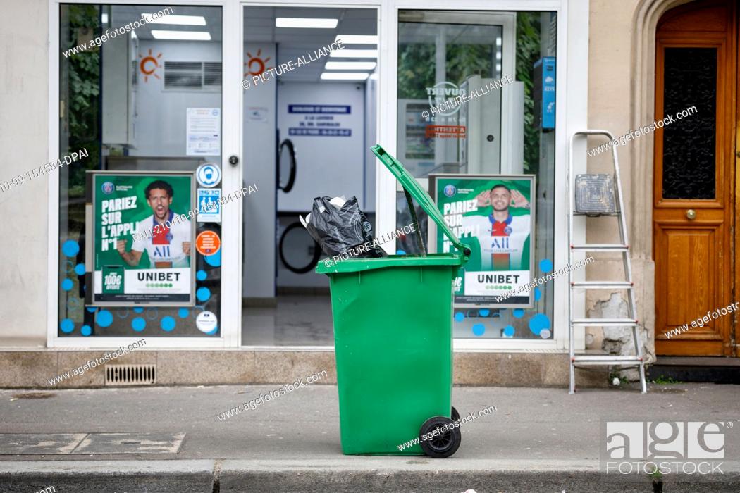 Stock Photo: 09 April 2021, France, Paris: A garbage can stands in front of a laundromat in the 15th district of Paris. Bulky waste on the sidewalk, overflowing garbage cans.