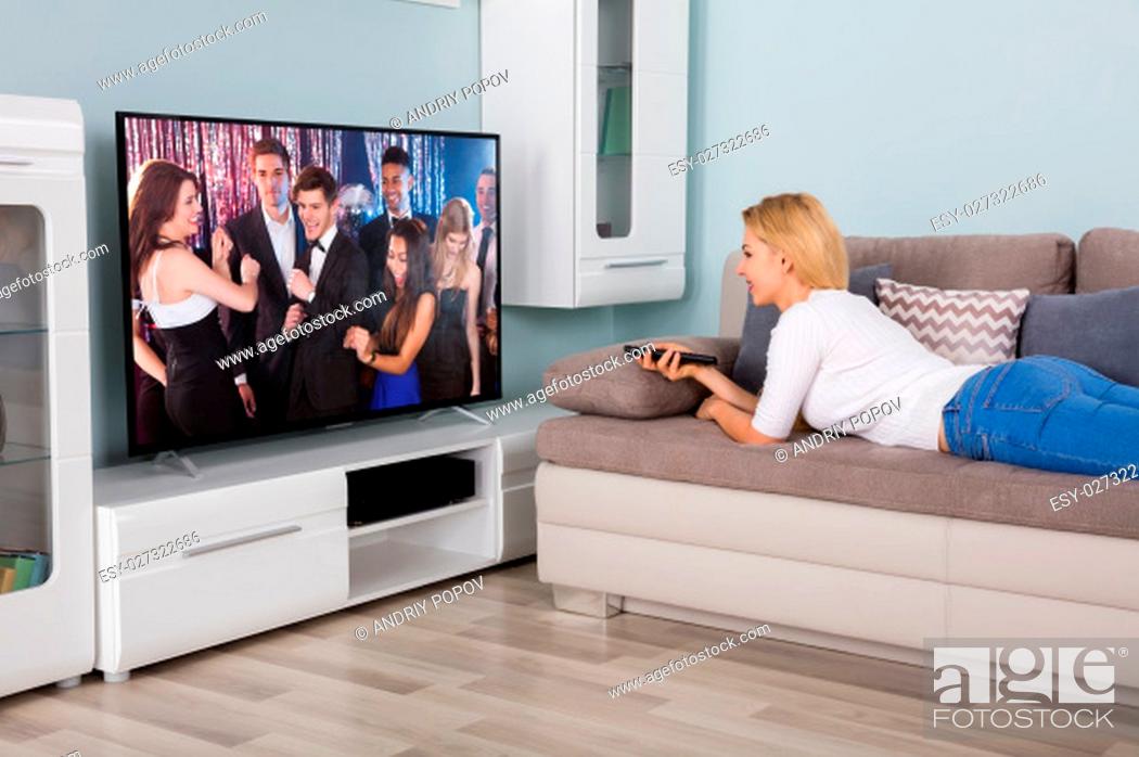 Stock Photo: Young Woman Lying On Sofa Watching Movie On Television At Home.